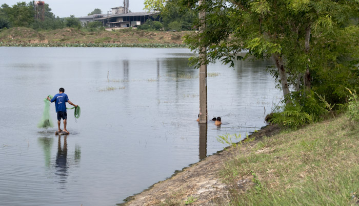 man fishing in lake from post