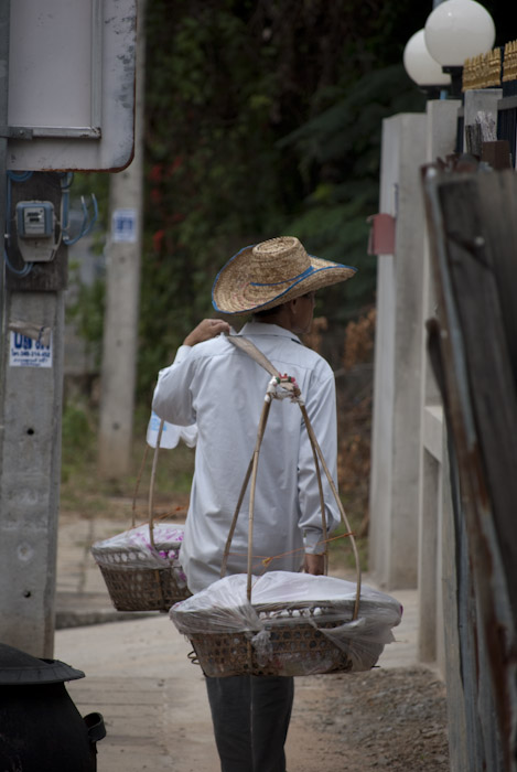 man carrying baskets on bar